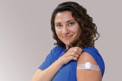 A woman lifts her t-shirt sleeve to show a bandage covering her flu shot injection.