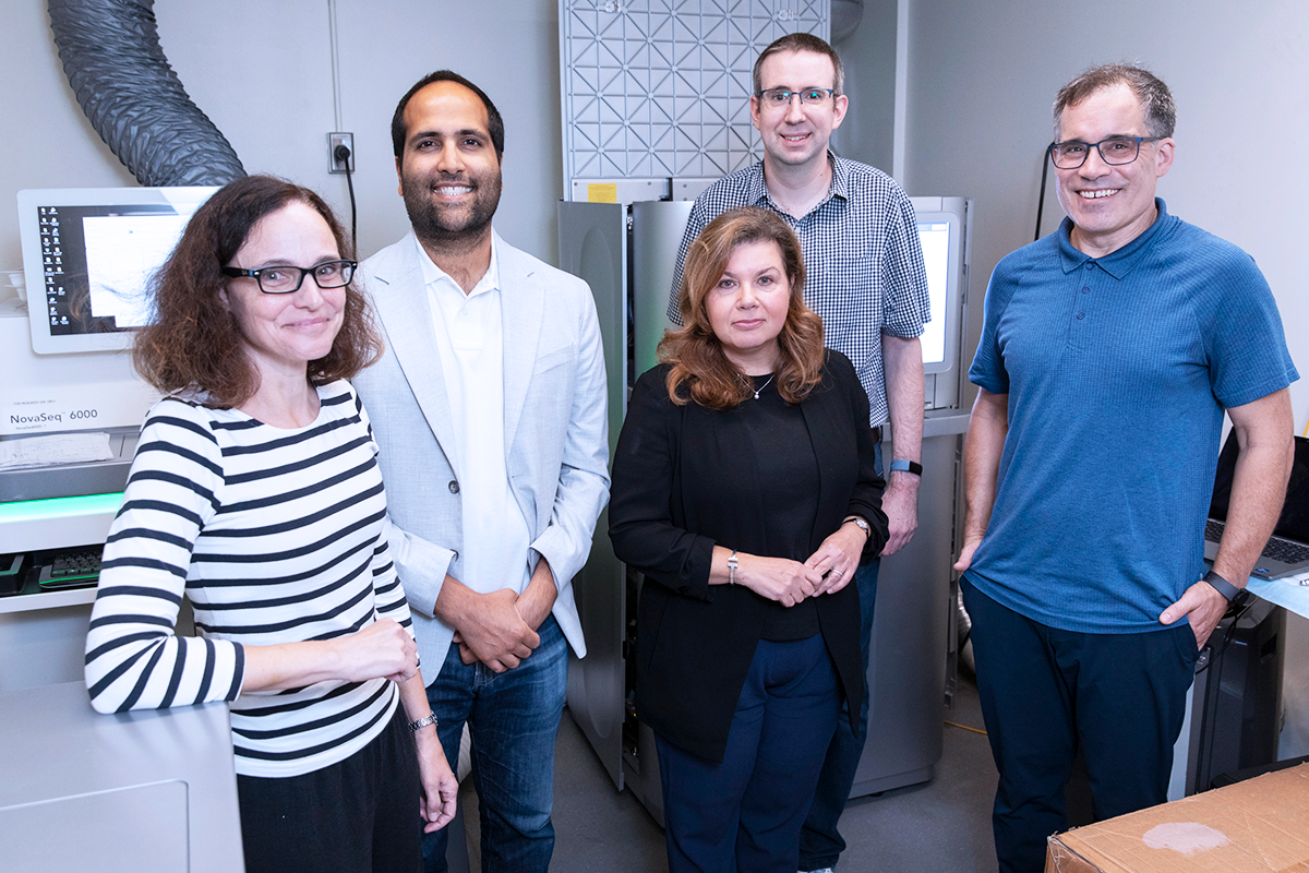 Five research project leads stand infront of a clinical RNA sequencer at SickKids.