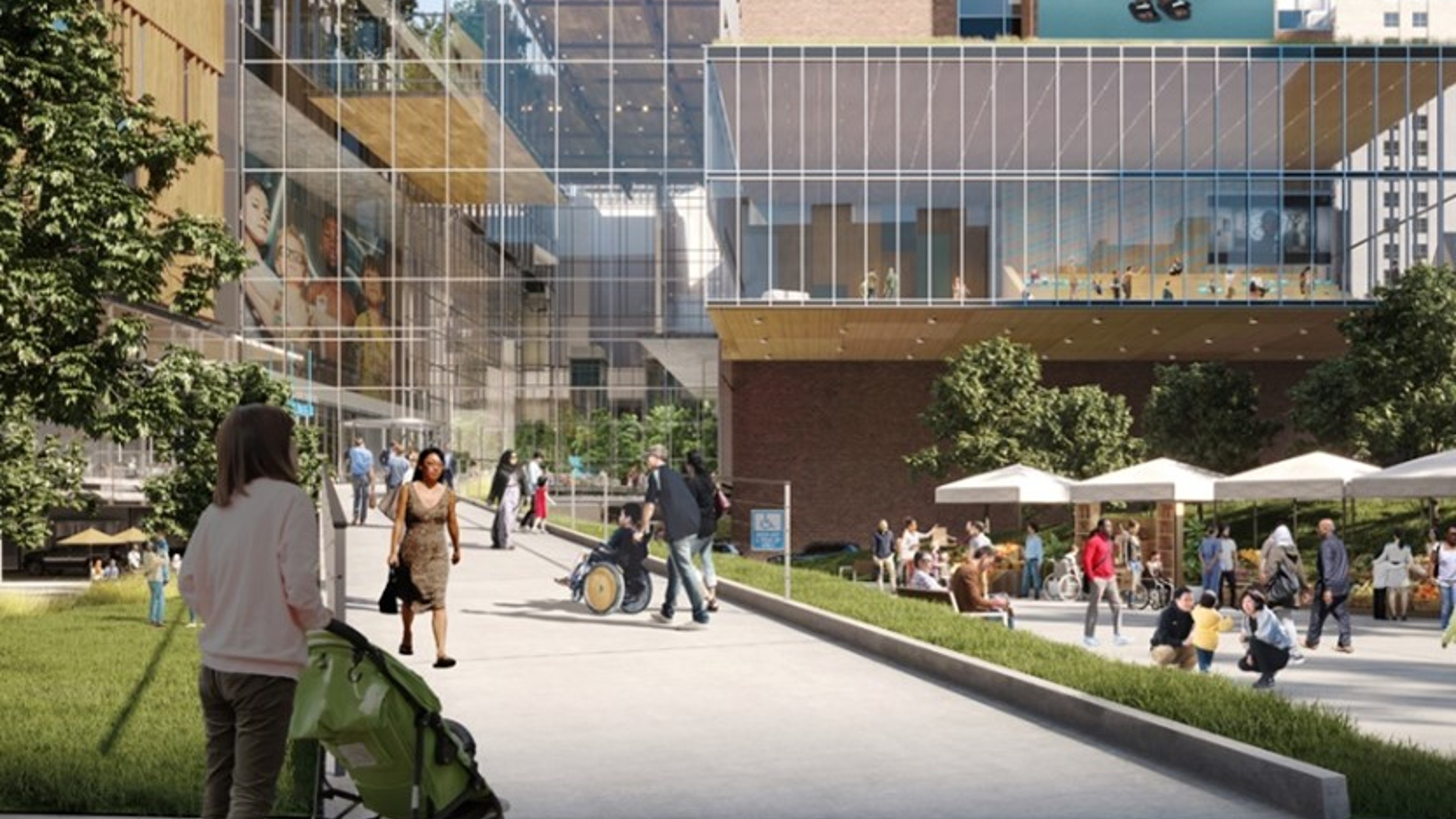 People walk and sit in an open plaza beside a modern glass building with trees, outdoor tables, and wide pathways.