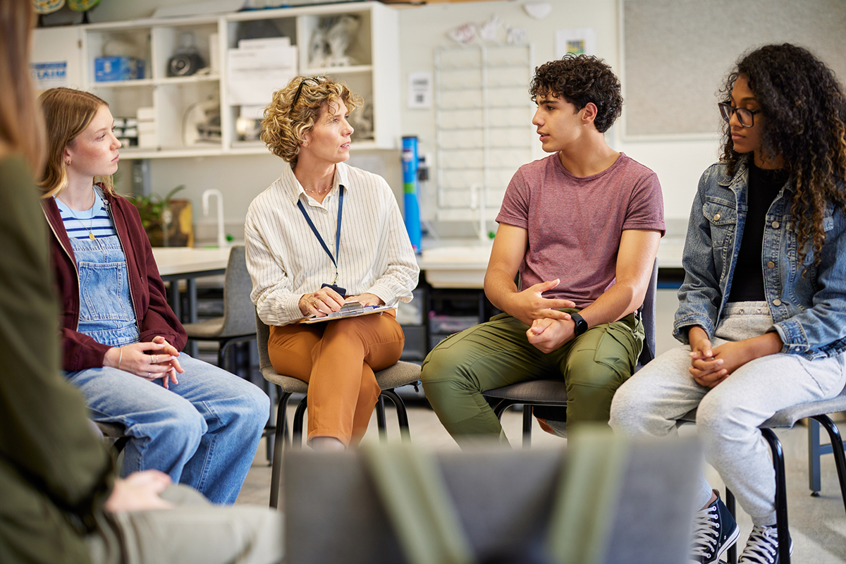 Youth and an adult with a clipboard talking in a circle.