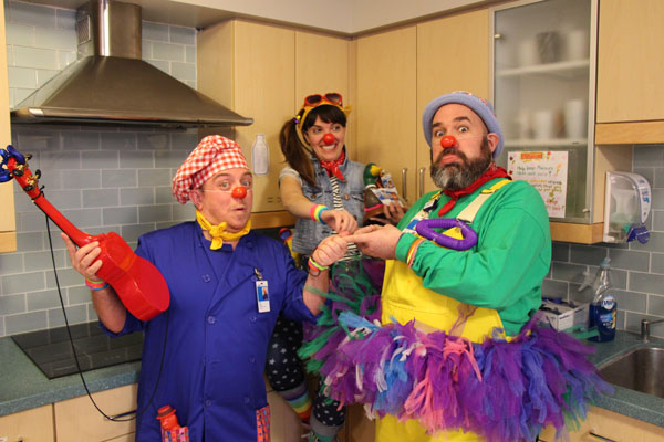 Three clowns pose together making funny faces.