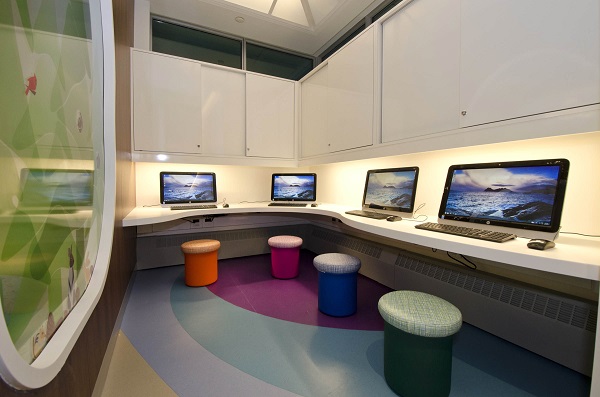 Four computers laid out on a corner desk, each with a stool.