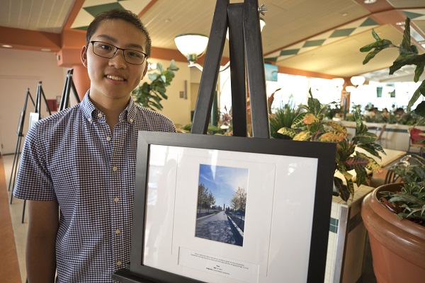 Teen boy stands next to framed image on an easel.