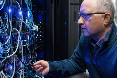 Andrei Turinsky approaches a series of blue wires connected to servers at SickKids.