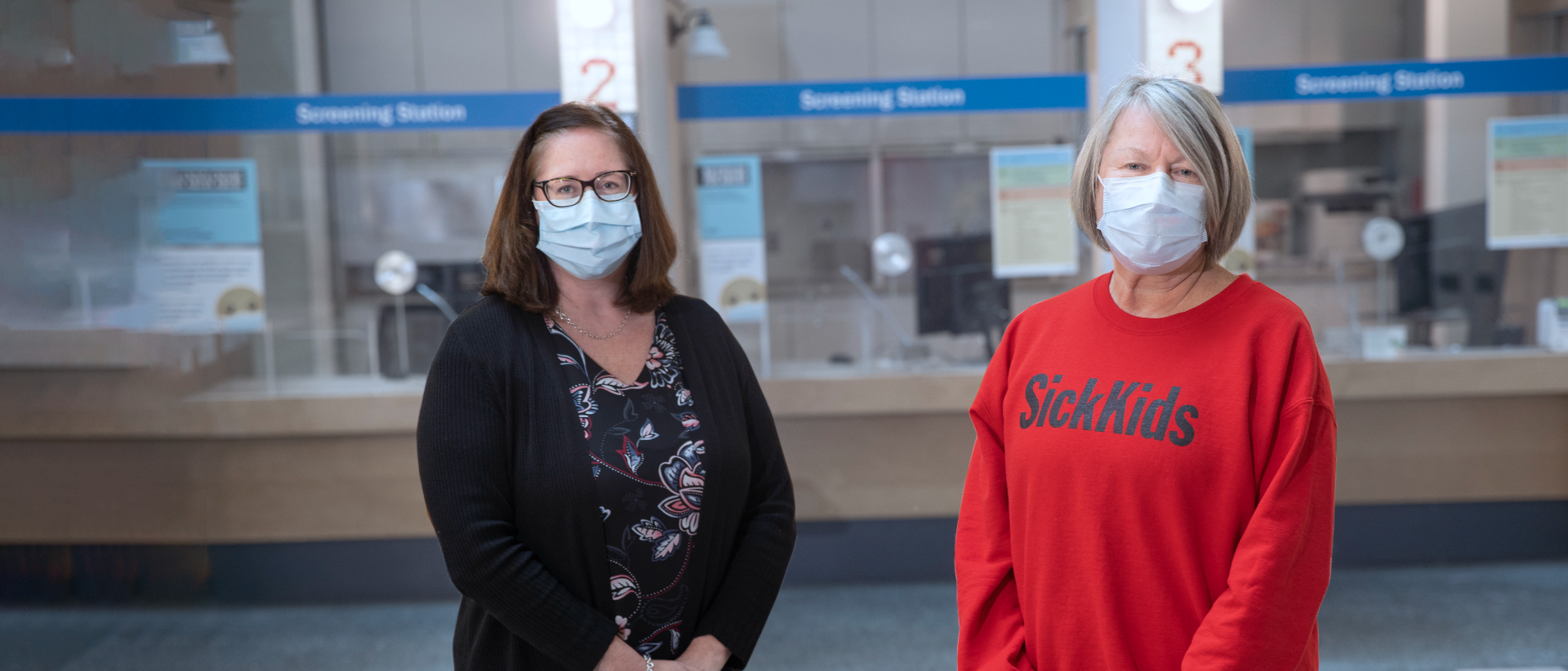 Stephanie Gracon-Lappan and Jane Ciordas-Lowes in masks. They are standing in front of the hospital screening stations.