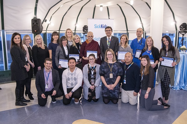 Group of staff stand together, some hold framed certificates.