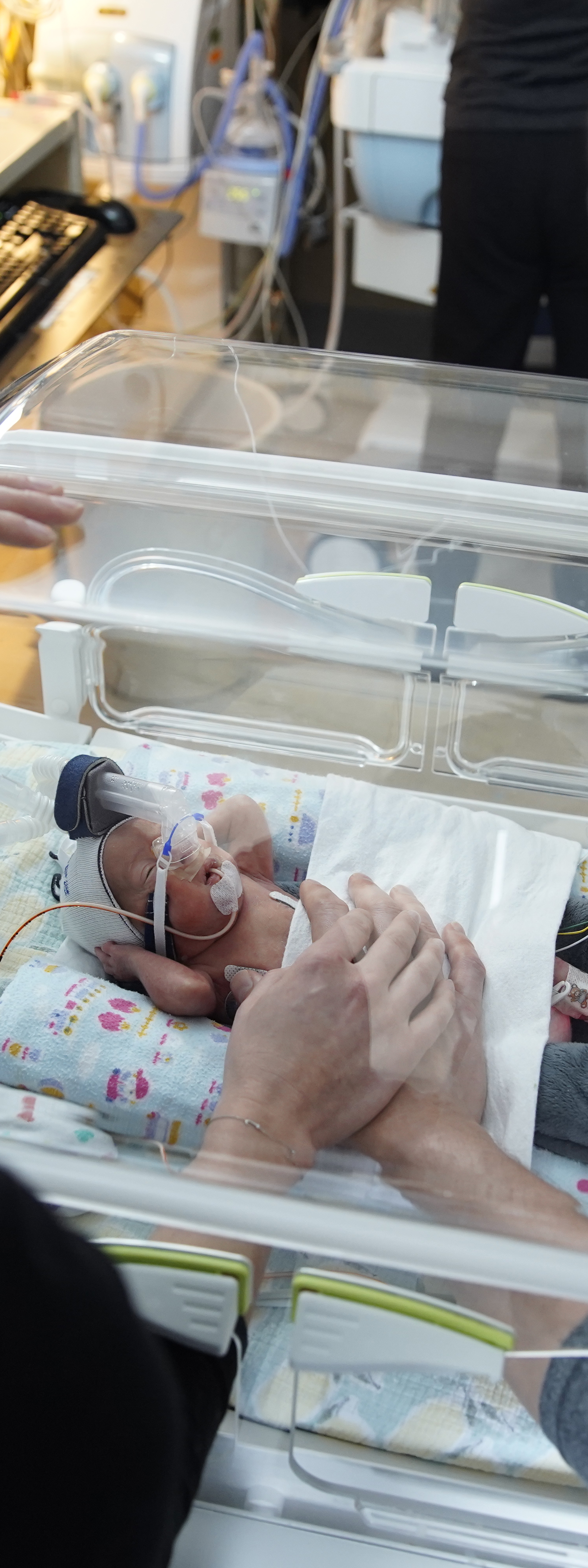 Erica and Brett in the SickKids NICU standing with Jeff in an incubator.