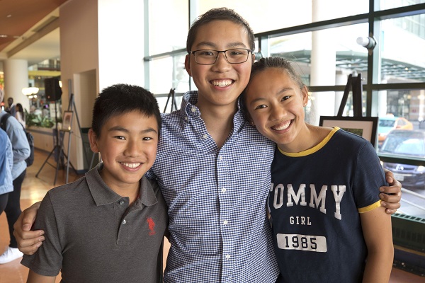 Three children stand with their arms around each other.