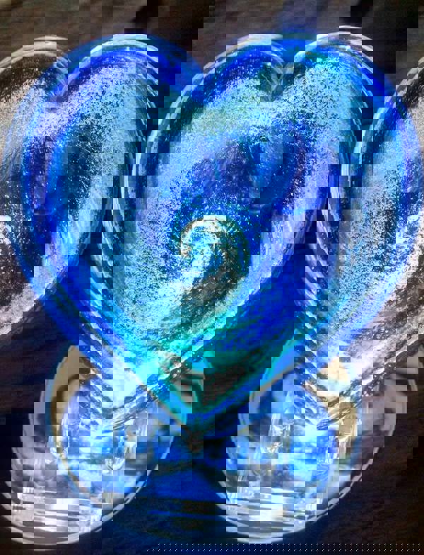 A glowing blue glass heart with ash design inside