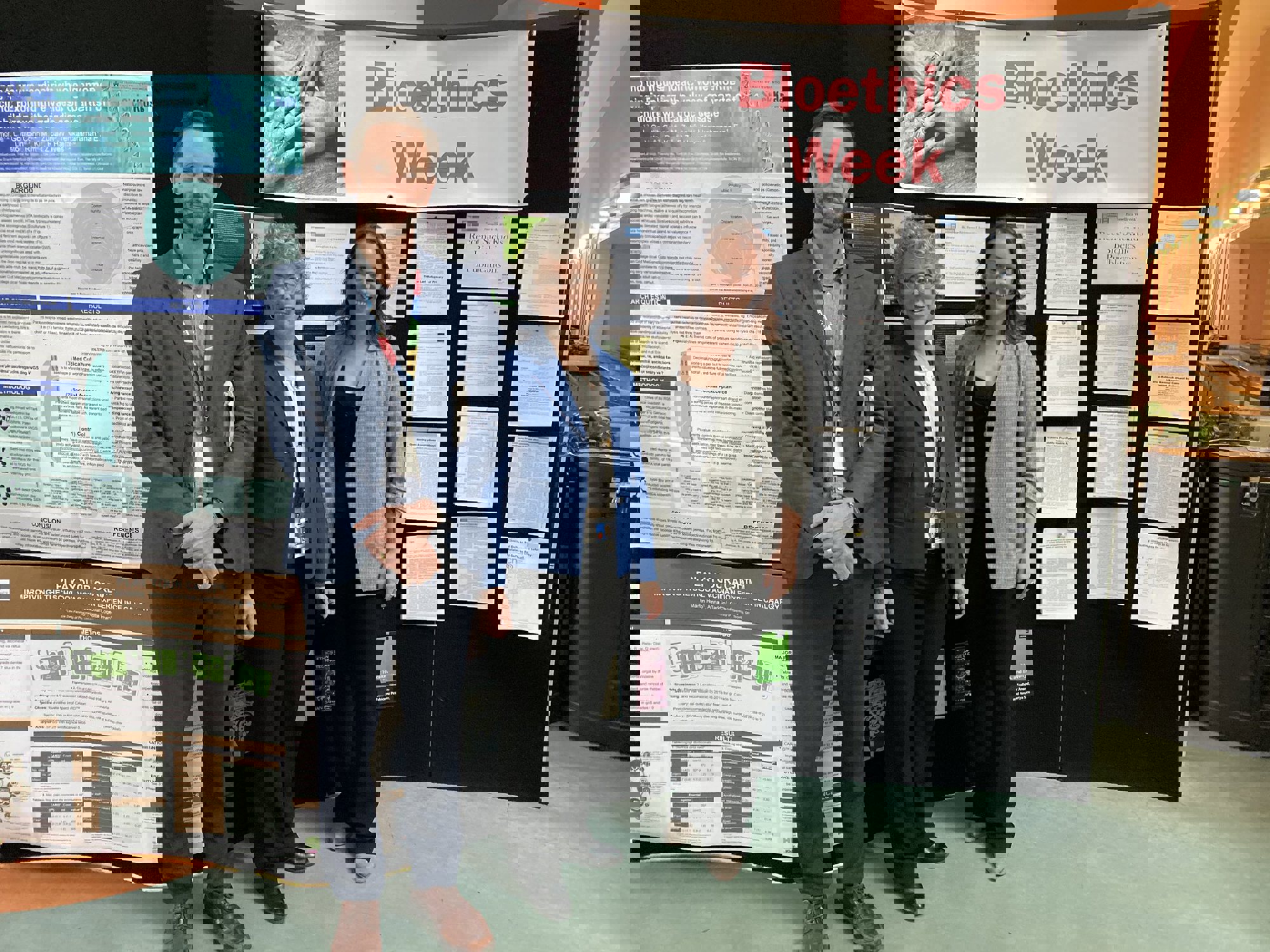 Three staff stand together in front of a poster display with a banner that reads Bioethics Week in the background.
