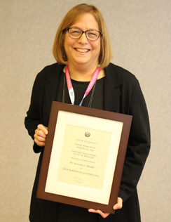 Barb Muskat smiles as she holds a framed plaque