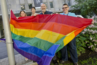 A group of four people standing at the bottom of a flag pole holding the Pride Flag at SickKids