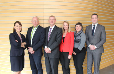 A group of 6 men and women in suits stand together 