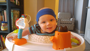 Baby wearing a headband in an exersaucer.
