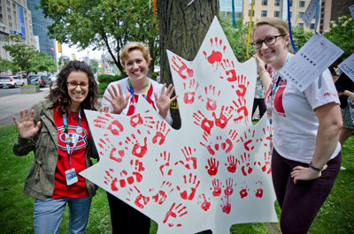 Staff stand around a white maple leaf with red handprints painted on it.