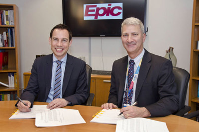 Two men sign papers while seated at a table.