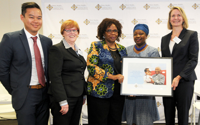 Group of five people stand together, two hold a framed certificate.