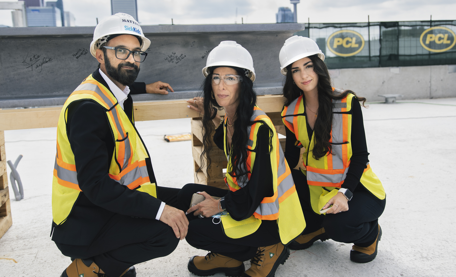 A man, woman and teenage girl wearing construction gear crouch down in front of a large steel beam covered in signatures