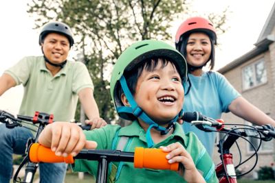 A man, girl and young boy ride bicycles and scooters. They all wear helmets.