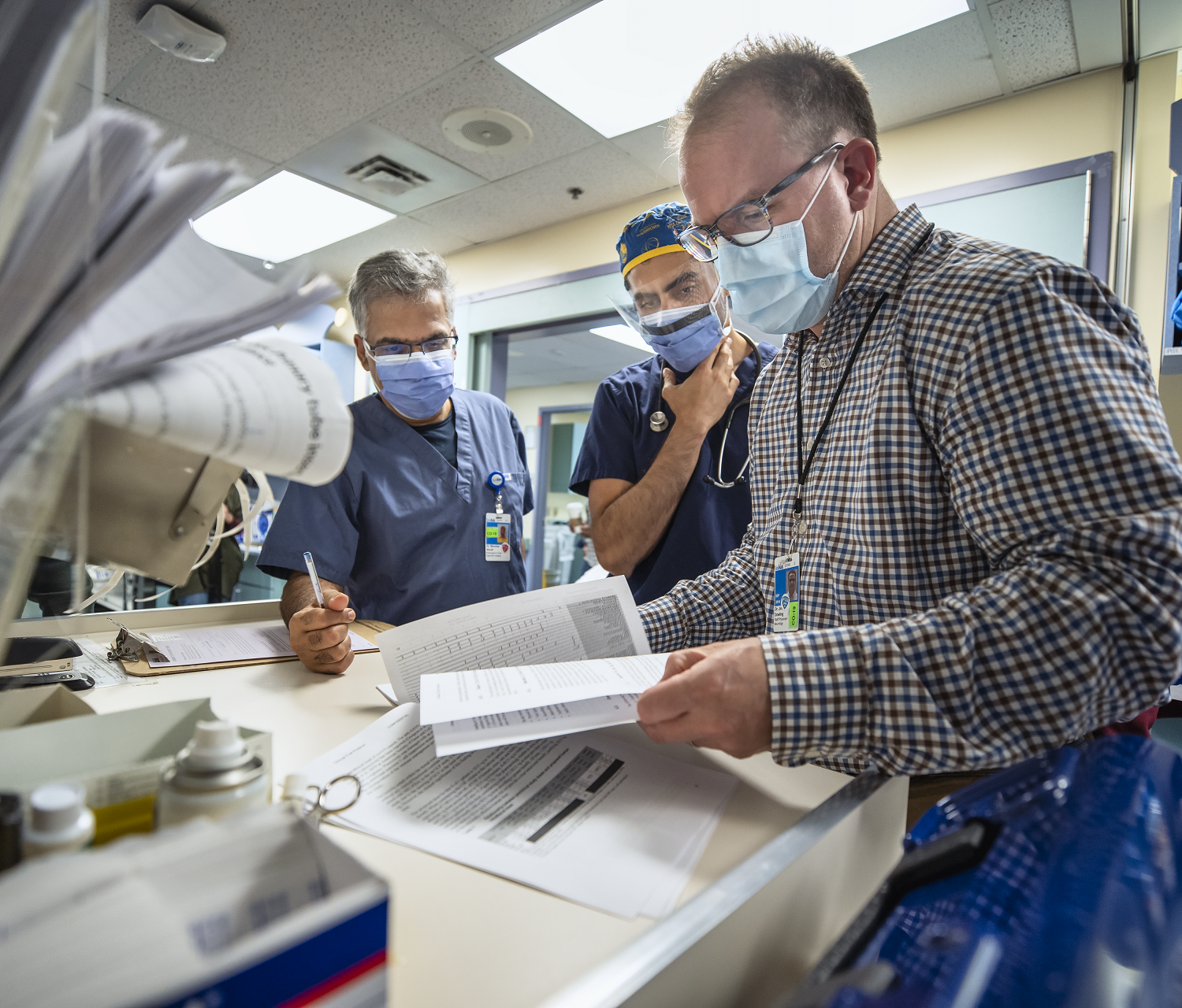 Three people stand together reviewing a document. They wear hospital masks and eye protection.
