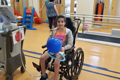 Child seated in a wheelchair connected to a large machine.