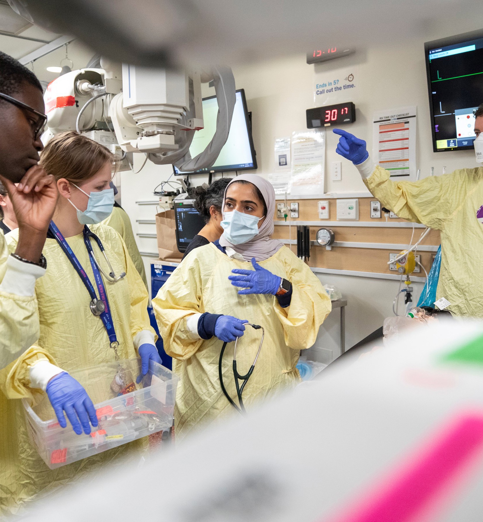 A care team conversing with each other, assesses their simulated patient in the trauma room.