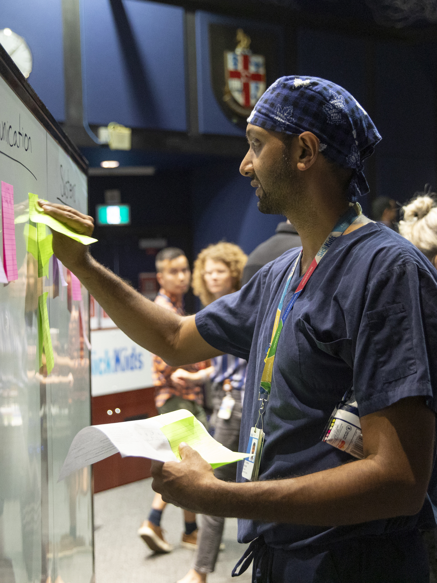 Dr. Joshua Ramjist reviews notes made by staff regarding areas for discussion during the Code Orange simulation debrief session in front of a white board full of sticky notes.