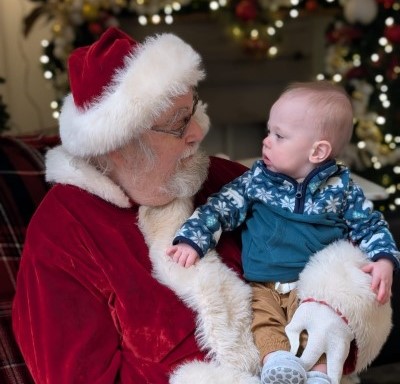 Santa holds Jeff in front of Christmas lights and decorations. 
