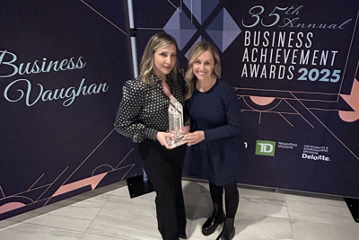 two women holding an award in front of an event backdrop