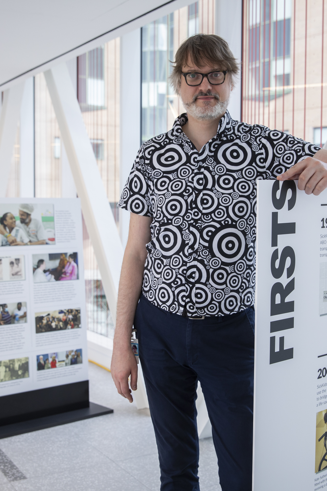Man in patterned black and white shirt standing next to timeline display showing historical events.