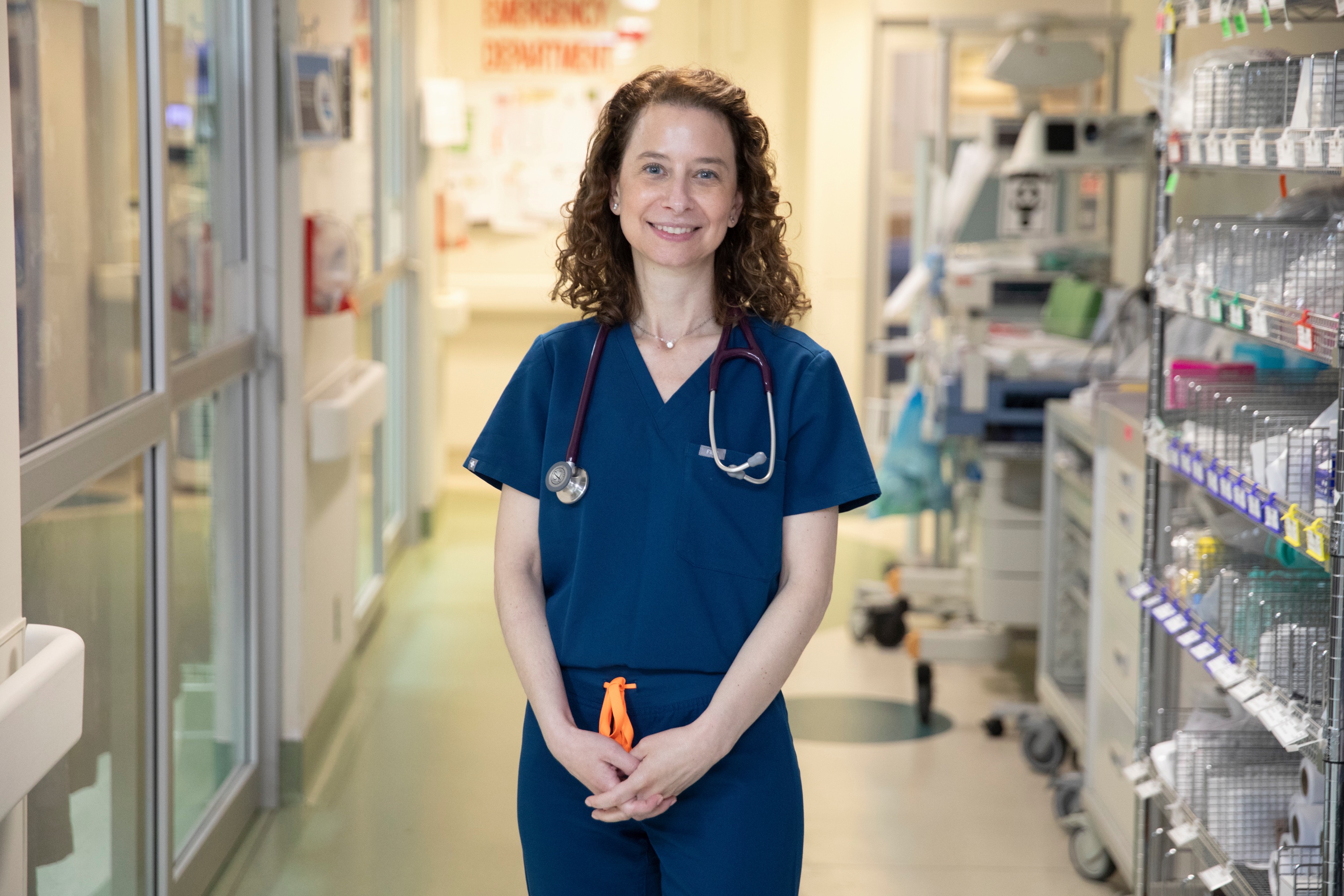 Dr. Deborah Schonfeld, wearing blue scrubs, stands in a hallway in the emergency department.