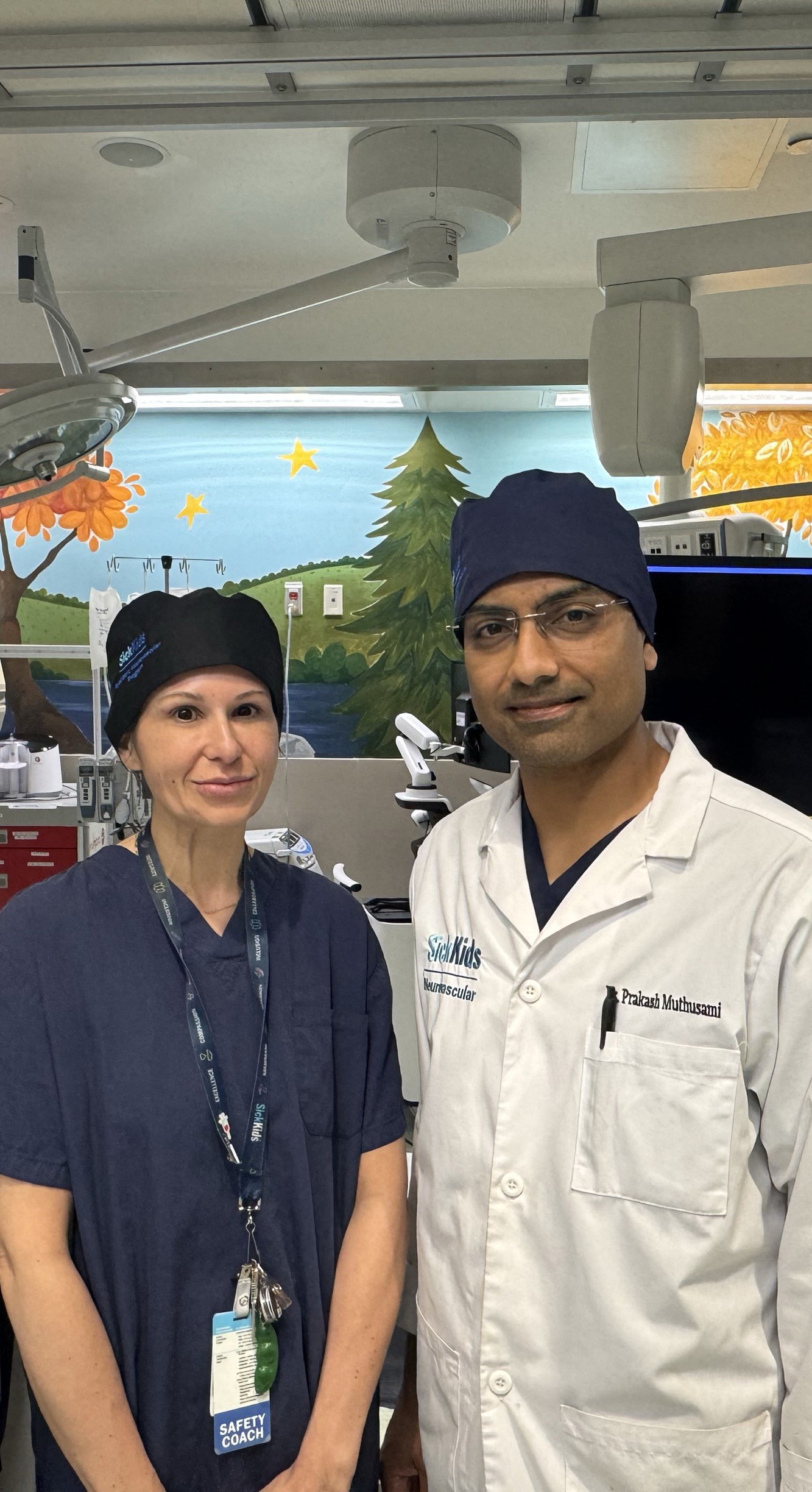 Three medical professionals posing in pediatric catheterization laboratory with colorful nature-themed wall murals and Siemens imaging equipment.