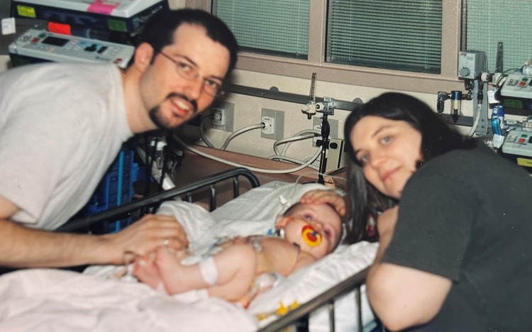 Six-month-old Liv post-surgery with her mom and dad on either side of her bed.