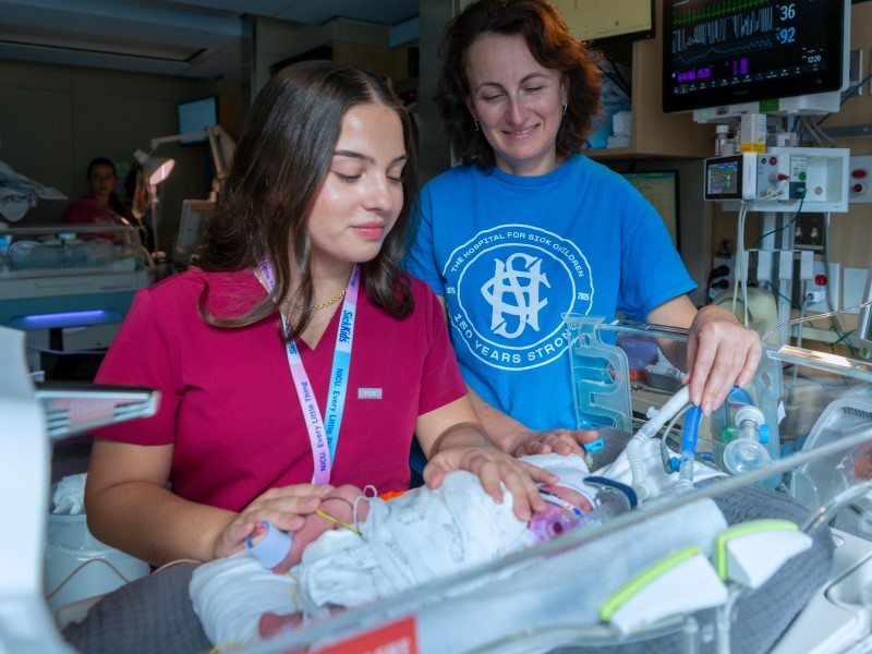 Franze and Yevel both tend to and look down at a baby in an incubator in the NICU.