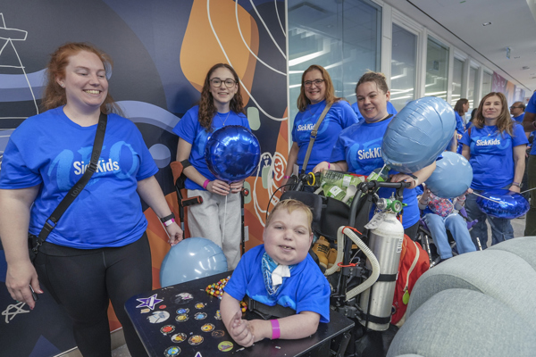 A group of SickKids 150 parade participants smiling and dressed in blue SickKids 150 t-shirts and holding blue balloons.