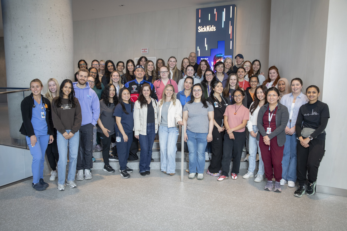 group shot of ED team standing together indoors on steps of the PSC lobby space with a digital display behind them.